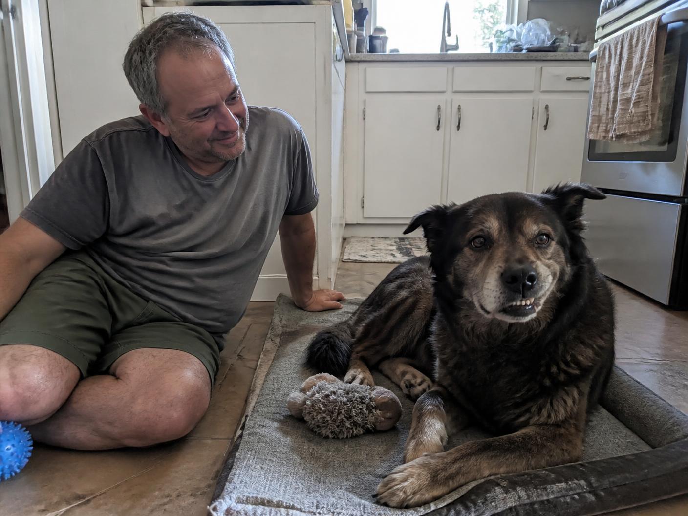 A man relaxing at home beside his older mixed-breed dog resting calmly on a mat